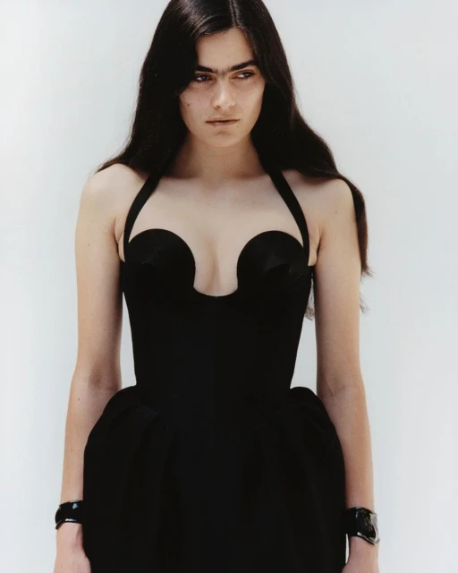 Elegant woman in a black halter dress against a white background, showcasing a minimalist fashion aesthetic and stylish wrist accessories.