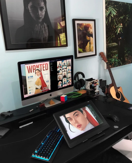 Workspace setup with computer screens displaying creative content, surrounded by art, keyboard, drawing tablet, and artistic tools.