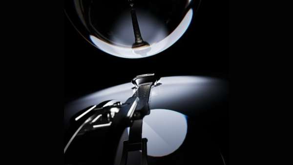 Close-up of a silver metal electric shaver on a stand, dramatically lit against a dark background with a round light overhead.