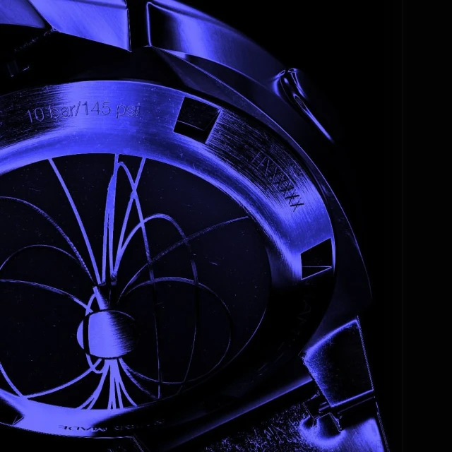 Close-up of a watch case back with engraved text and a radial pattern in shades of blue against a dark background.