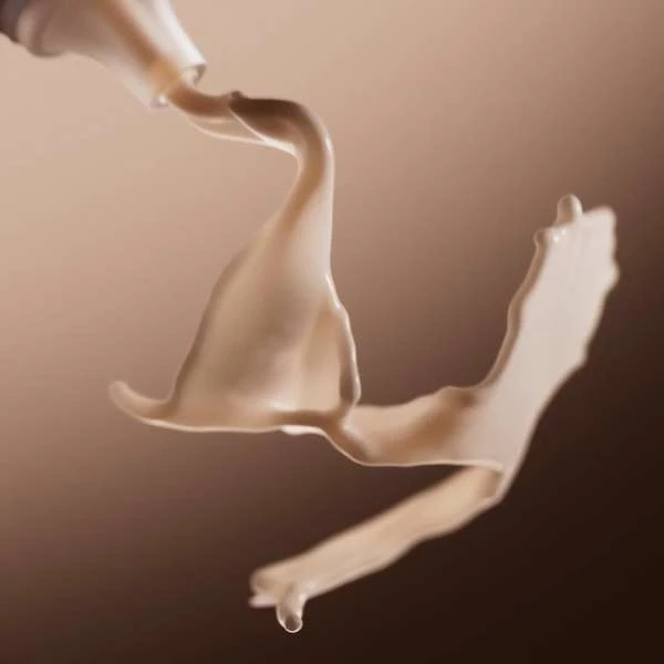 Abstract studio shot of viscous liquid flowing from a white tube against a tan backdrop, creating dynamic shapes and movement.