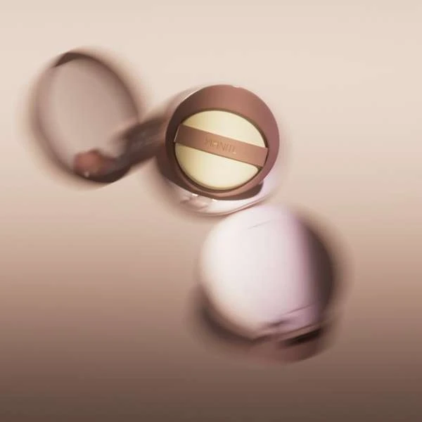 Beauty shot of a cosmetic compact with blurred motion, on a tan surface, focusing on the product's design and aesthetic appeal.