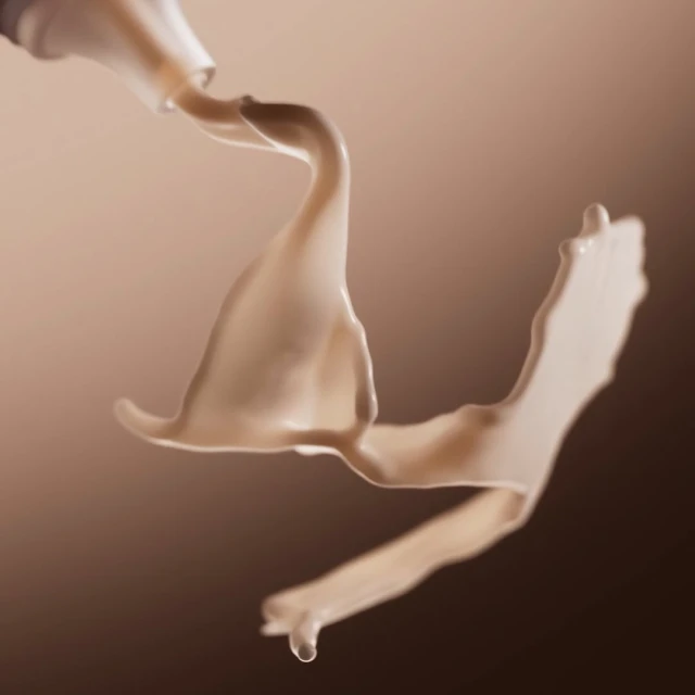 Creamy beige liquid flows from a tube, showcasing its smooth texture and color against a gradient backdrop, highlighting a beauty or cosmetic product.