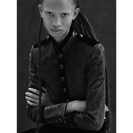 Portrait of a Black woman with dreadlocks, wearing a dark velvet jacket with button details, shot in black and white.