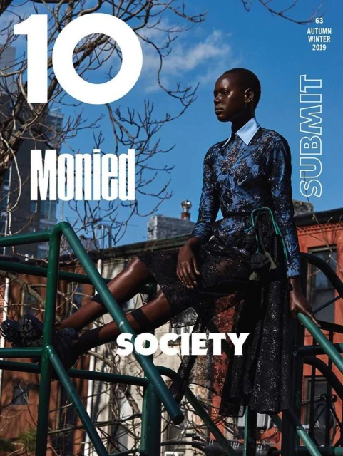 Magazine cover featuring a Black female model in patterned dress, posing on green metal playground structure against an urban and sky background.
