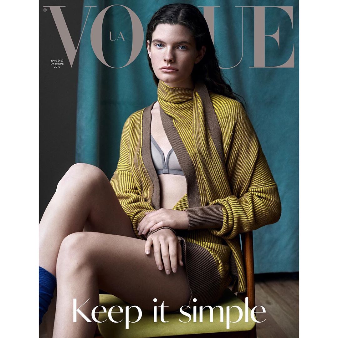Fashion magazine cover featuring a female model in a yellow and brown knit cardigan and bra sitting on a green chair in a studio.