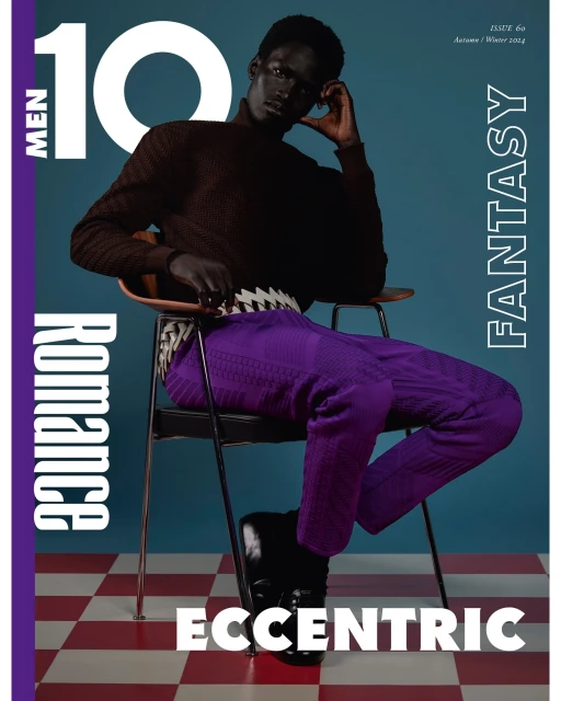 Magazine cover featuring a seated Black male model in a brown sweater and purple pants on a checkered floor against a blue backdrop.