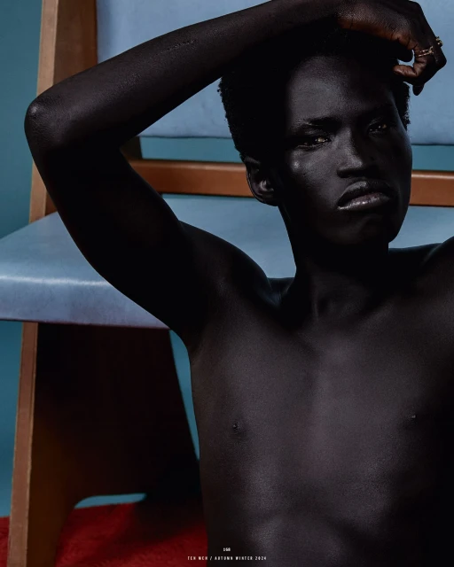 Studio shot of a Black adult with an up-close view, accented with a chair in the background, capturing an essence of minimalistic fashion.