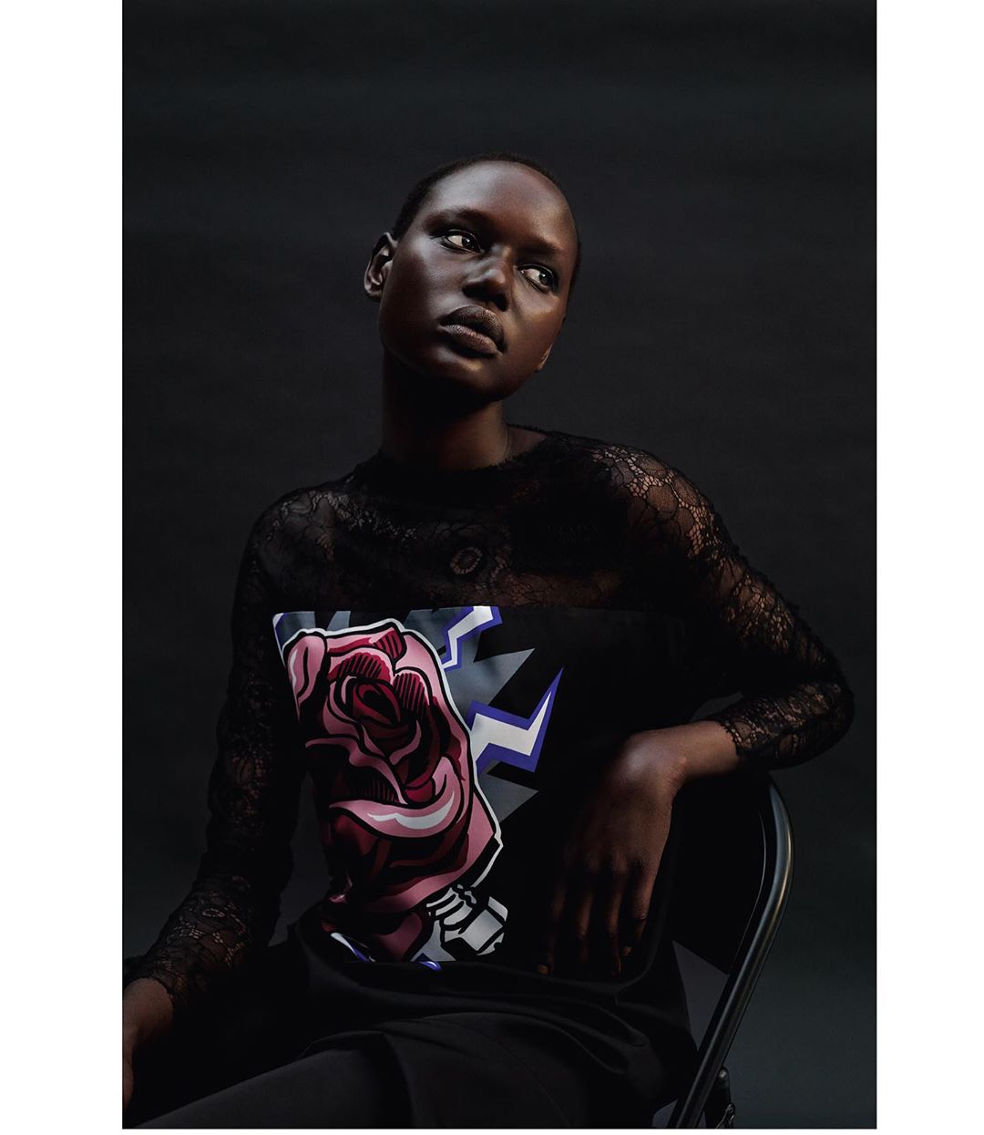 Portrait of a black woman with a rose graphic on her shirt, looking up in a studio against a dark background with low-key lighting.