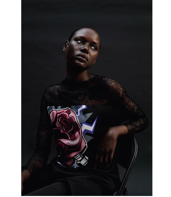 Portrait of a black woman with a rose graphic on her shirt, looking up in a studio against a dark background with low-key lighting.