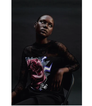 Portrait of a black woman with a rose graphic on her shirt, looking up in a studio against a dark background with low-key lighting.