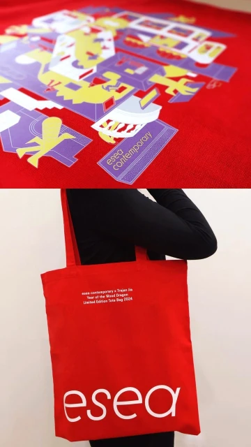 A red tote bag with the logo 'esea' in white is held by a person wearing black, with a colorful design on a red background above.