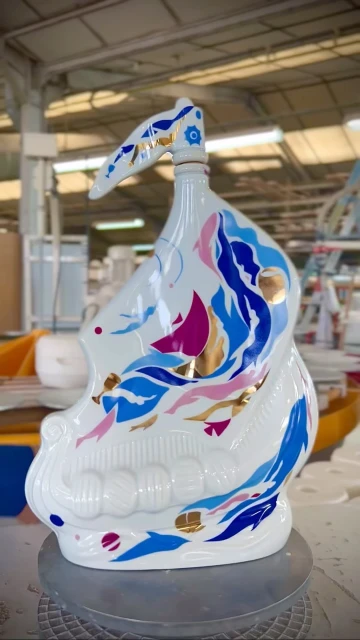 Intricate porcelain bottle featuring blue, pink, and gold designs in a studio setting, showcasing craftsmanship and artistic design.