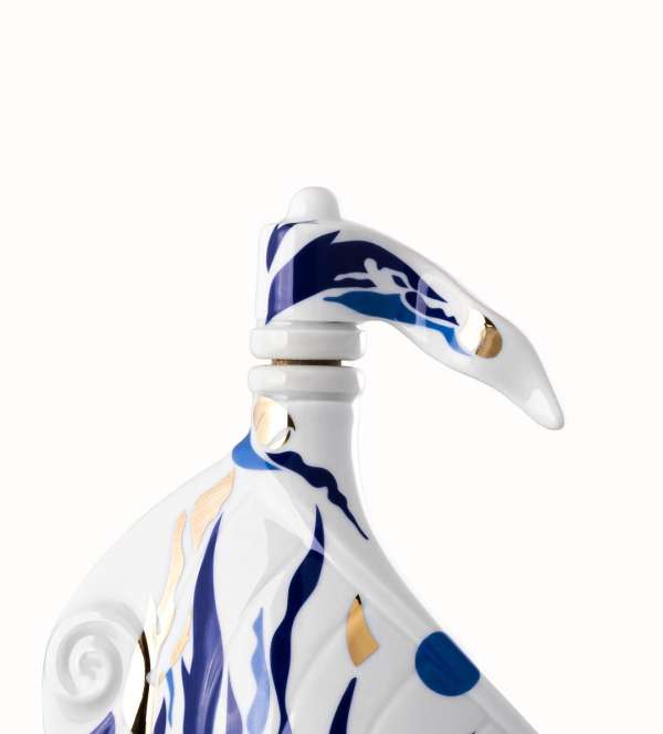 Close-up of a white porcelain piece with blue wave patterns and a figure; artistic nautical-themed design on a clean, white background.