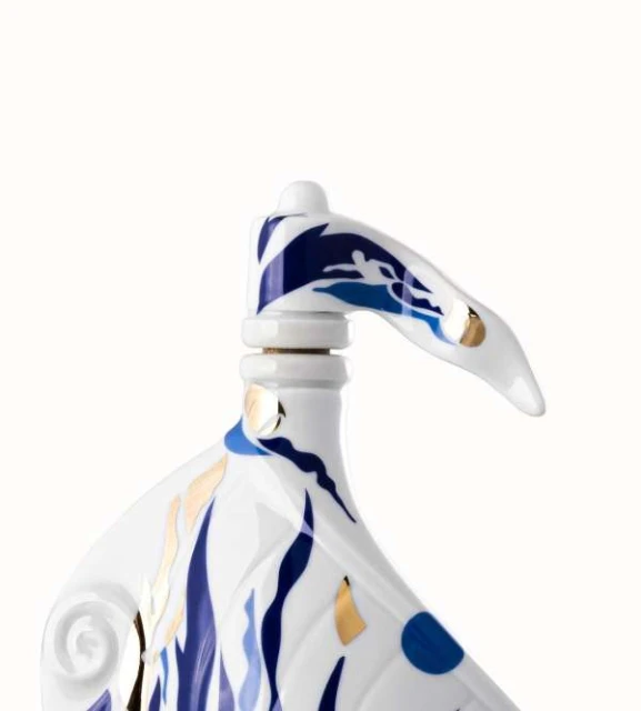 Close-up of a white porcelain piece with blue wave patterns and a figure; artistic nautical-themed design on a clean, white background.