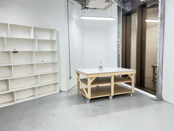 Minimalist white room featuring a wooden table with a white top, a white bookshelf, and neutral grey flooring.