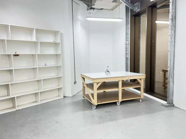 Minimalist white room featuring a wooden table with a white top, a white bookshelf, and neutral grey flooring.