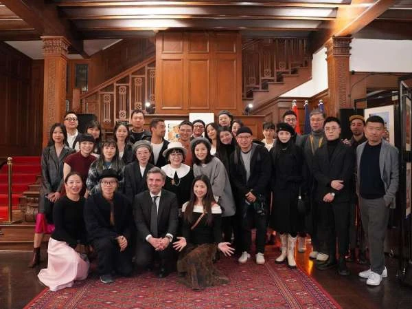 Large group of Asian and White people pose indoors in an ornate hall with a red carpeted staircase in the background for a group portrait.