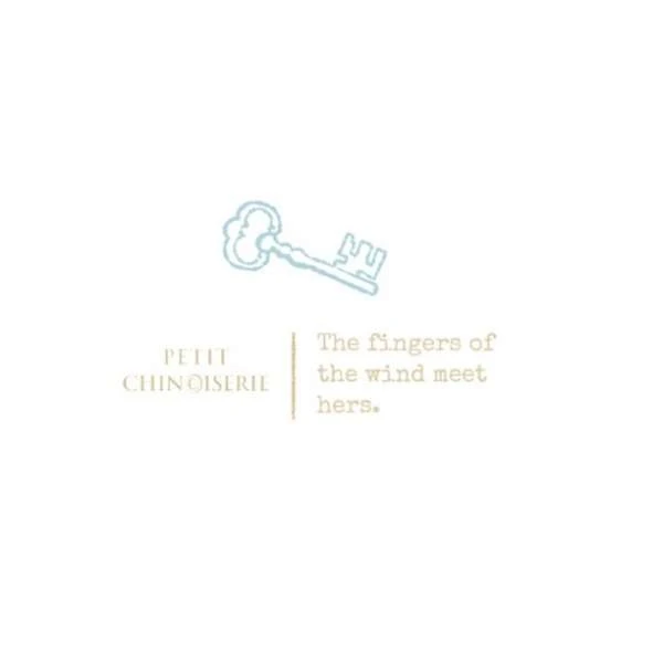 Conceptual art featuring a stylized key illustration with the text 'Petit Chinoiserie' and the poetic phrase 'The fingers of the wind meet hers'.