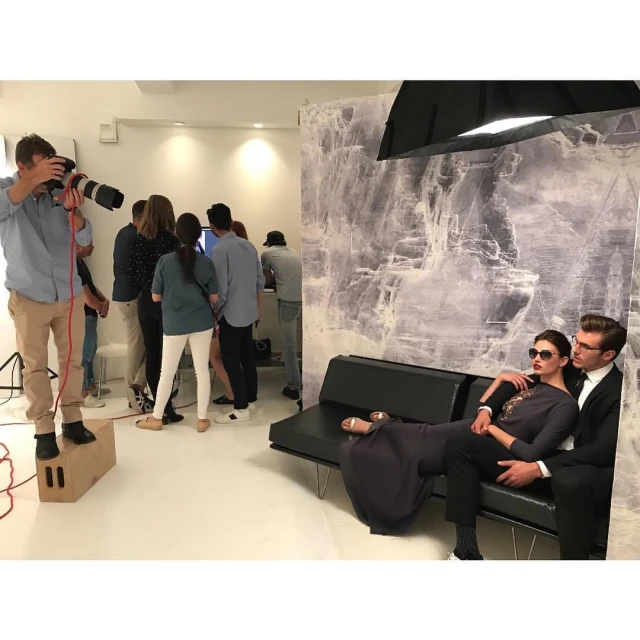 Fashion photo shoot in photo studio with a man and a woman modeling, a photographer, and photo crew in a bright indoor setting.