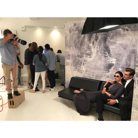 Fashion photo shoot in photo studio with a man and a woman modeling, a photographer, and photo crew in a bright indoor setting.