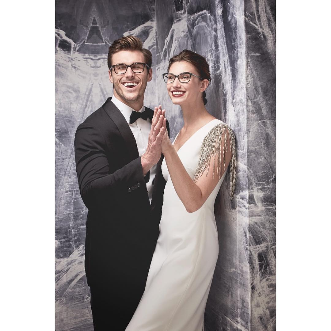 Elegant couple poses in formal wear and eyeglasses in a photo studio with a marble background. Smiling man and woman.