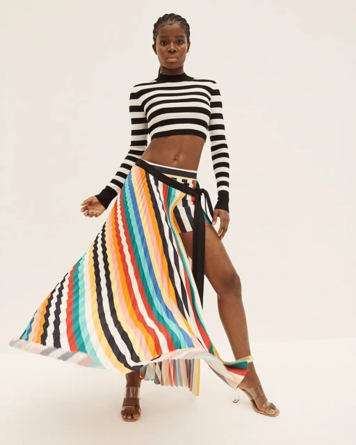 Fashion shot: A stylish Black woman poses in a striped crop top and vibrant rainbow skirt against a bright background in a studio setting.
