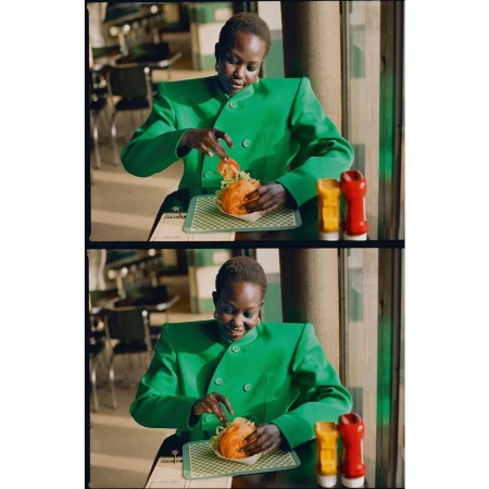 Woman in a green suit jacket sits at a diner table preparing to eat a burger with condiments, inside a retro-style restaurant.