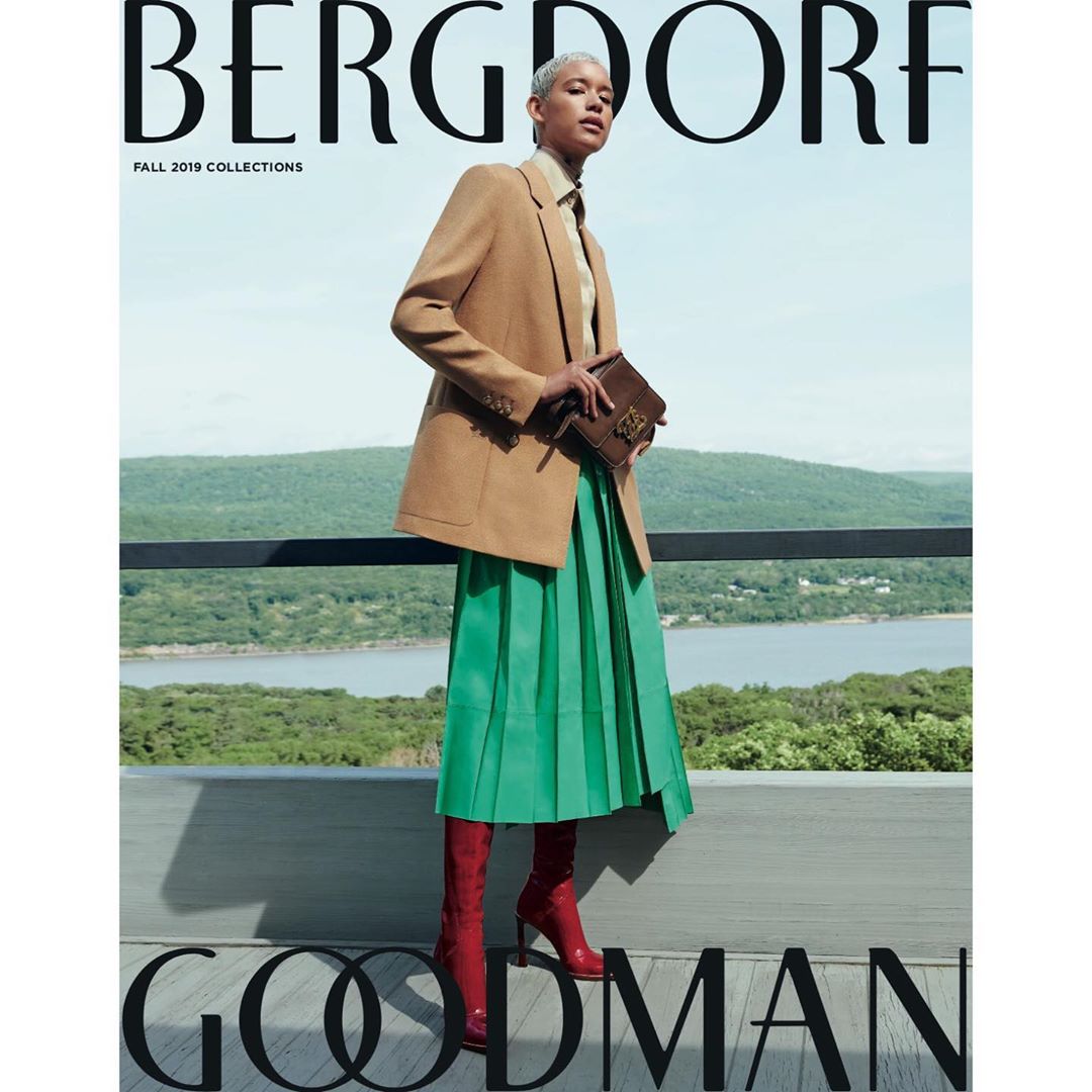 Magazine cover featuring a model in a tan blazer, green pleated skirt, and red boots, standing against a scenic outdoor background.