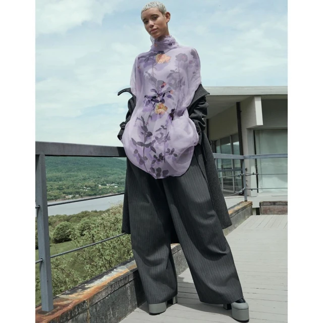 Fashionable woman in a lilac floral blouse and wide-leg pinstripe trousers posing outdoors near modern architecture.
