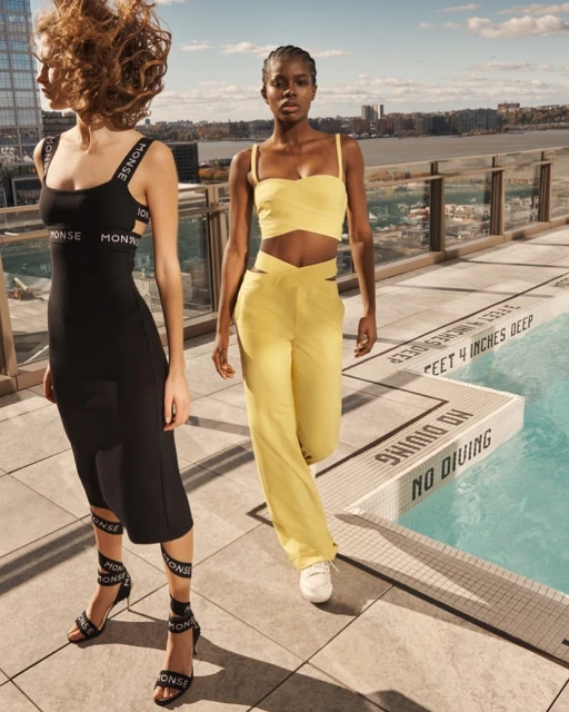 Two fashion models pose on a rooftop near a swimming pool and city buildings. One wears a black dress and heels, the other a yellow suit.