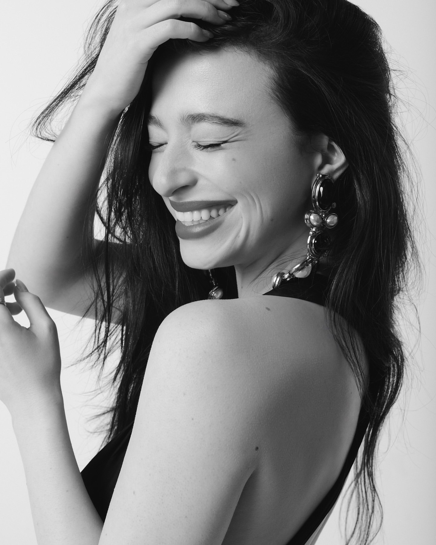 Black and white portrait of a smiling woman with long dark hair, wearing large earrings and a dark top, against a plain background.