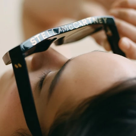 Close-up portrait of a person holding black sunglasses with branded lettering along the frame by Tiffany Nicholson.