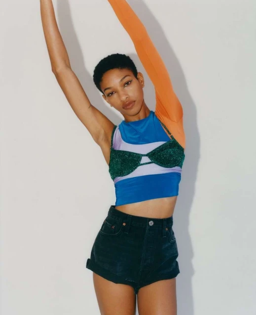 Fashionable woman in stylish top and shorts strikes a pose in a studio. The outfit features a unique design and bold color contrast.
