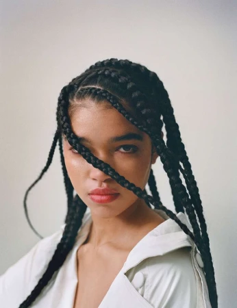 Portrait of a woman with long black box braids wearing an off-white shirt against a plain light background