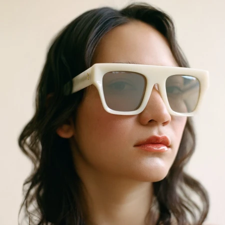 Close-up portrait of a woman wearing thick white statement sunglasses against a neutral background