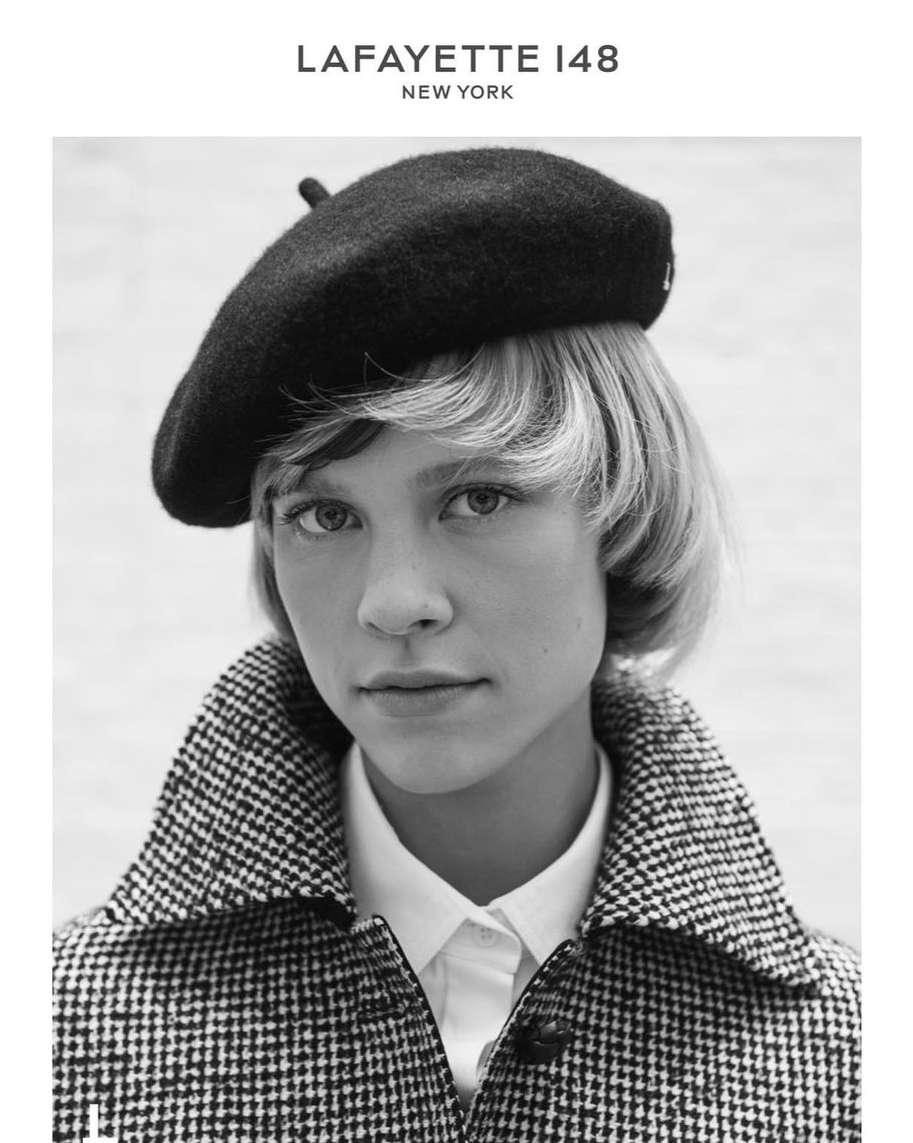 Black and white portrait of a fair-skinned young adult female with short blonde hair, wearing a black beret and patterned coat.