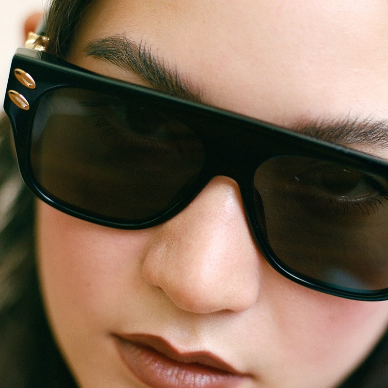 Close-up portrait of a person wearing thick black sunglasses with metallic stud details on the frames.