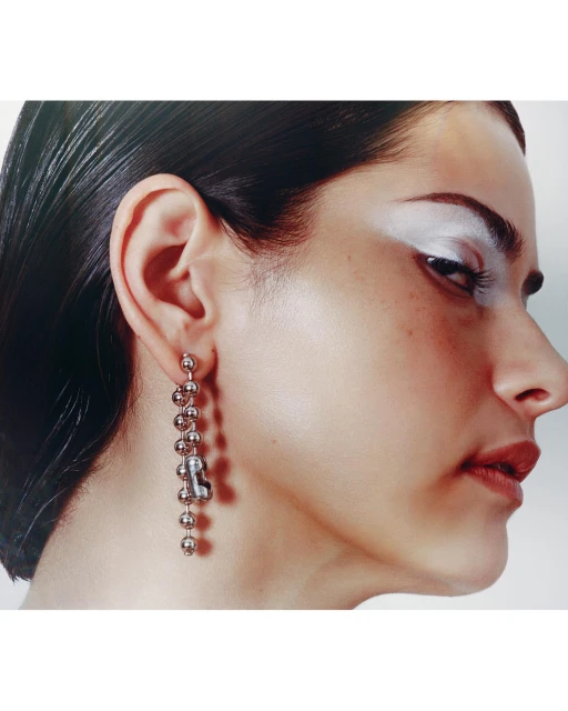 Woman with dark hair wearing a dangling earring and makeup in a close up studio shot with a white background.