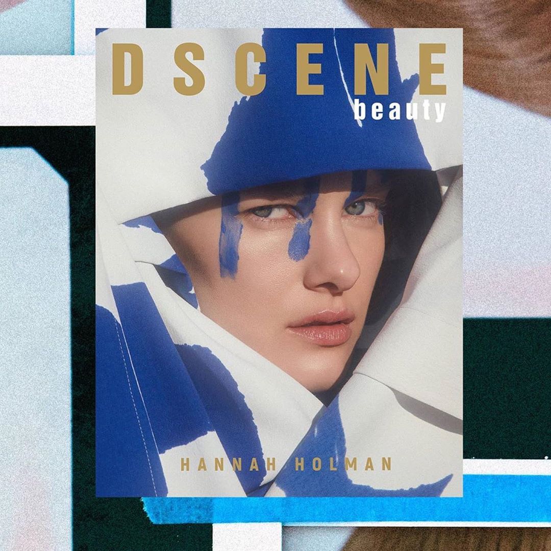 Magazine cover featuring a model with blue face paint wearing a white and blue jacket in a studio setting with geometric props.