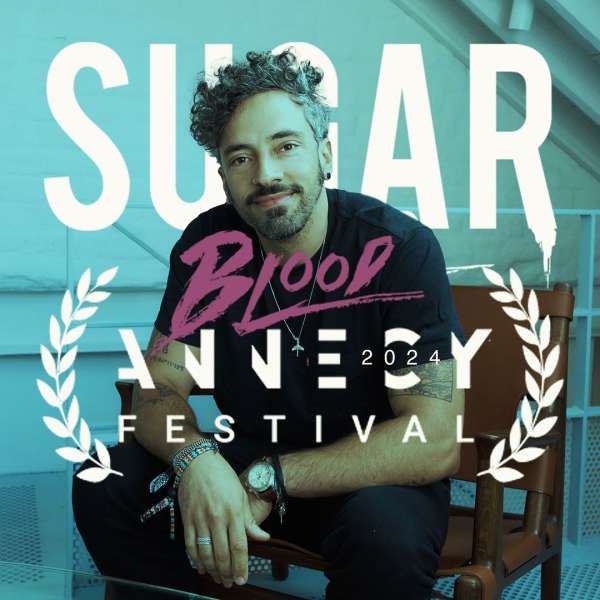 Adult male portrait sitting on a chair in front of graphic typography promoting 'Blood Sugar Annecy Festival 2024' against a blue background.