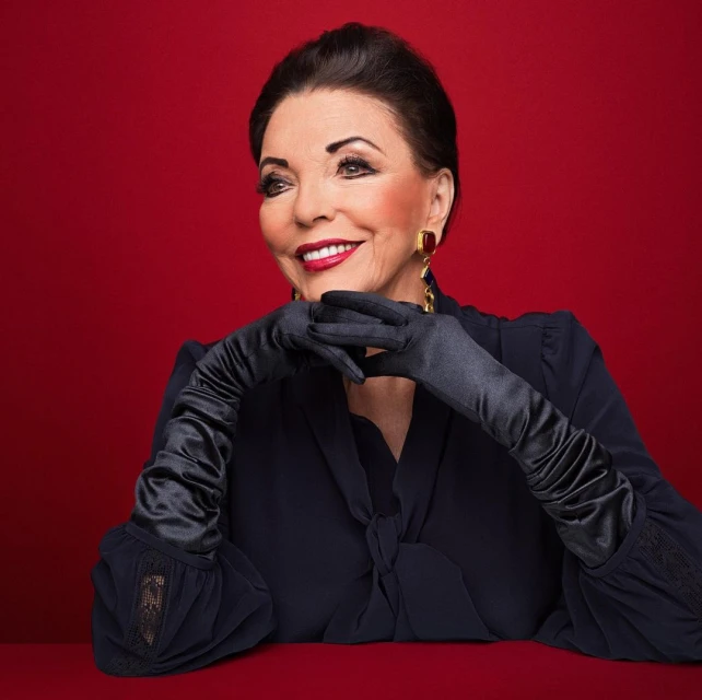 Elegant portrait of older woman with black hair and gloves against a red backdrop, featuring red lipstick, jewelry, and a sophisticated look.