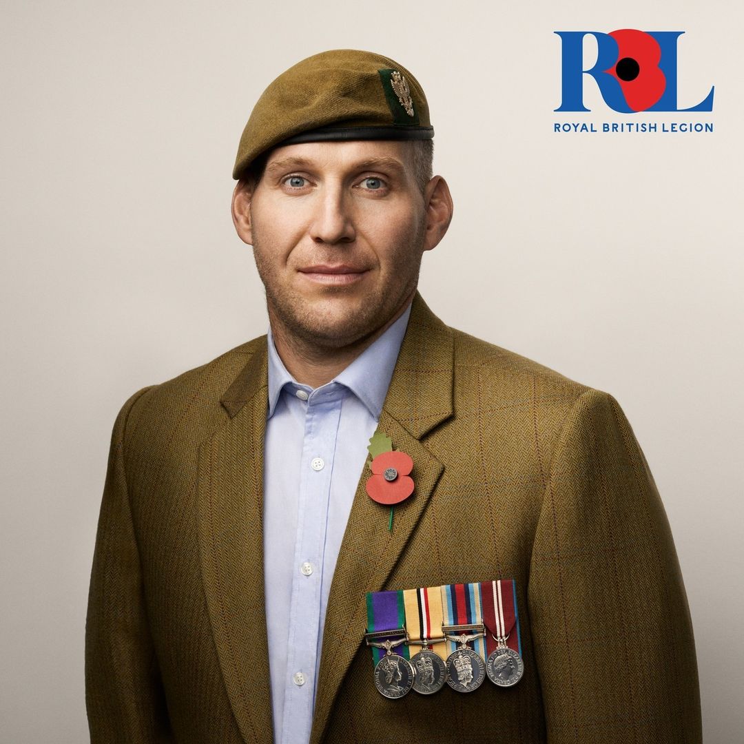Portrait of an adult male wearing a brown tweed jacket, blue shirt, and a tan beret, featuring military medals and a poppy pin. The background is white.