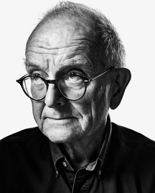 Black and white portrait of an elderly adult man with glasses in front of a white background, wearing a button-down shirt.