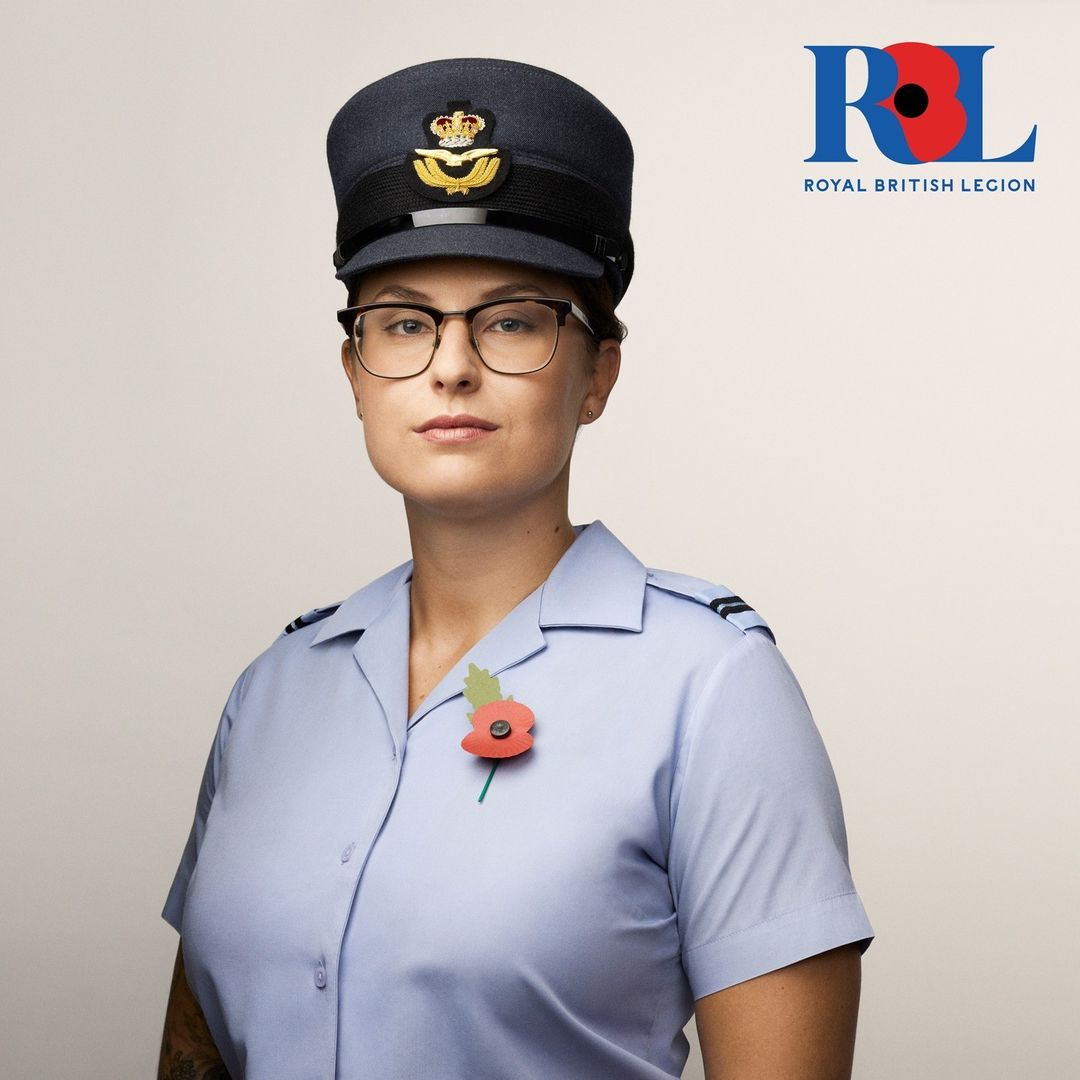 Portrait of woman in air force uniform and cap, wearing glasses and poppy pin. Royal British Legion logo visible in upper right.