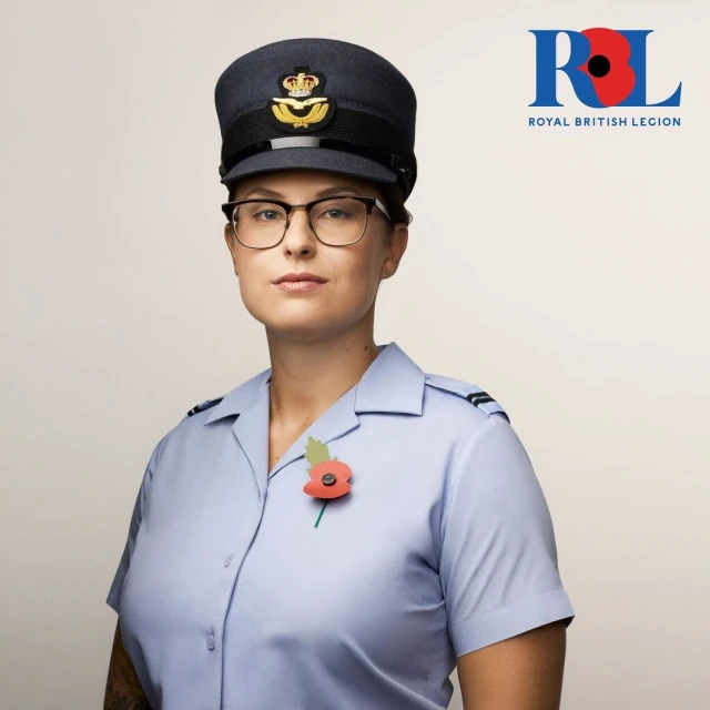 Portrait of woman in air force uniform and cap, wearing glasses and poppy pin. Royal British Legion logo visible in upper right.