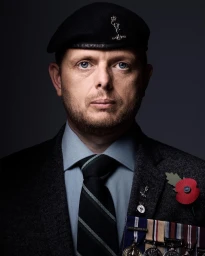 Portrait of a man in military beret and suit with medals and poppy pin against a grey background photographed by Stuart Mcclymont.