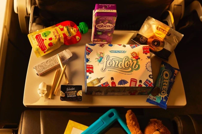 Airplane tray table with a variety of packaged snack foods, including fruit pouches, cookies, and cheddar cheese spread, on a flight.