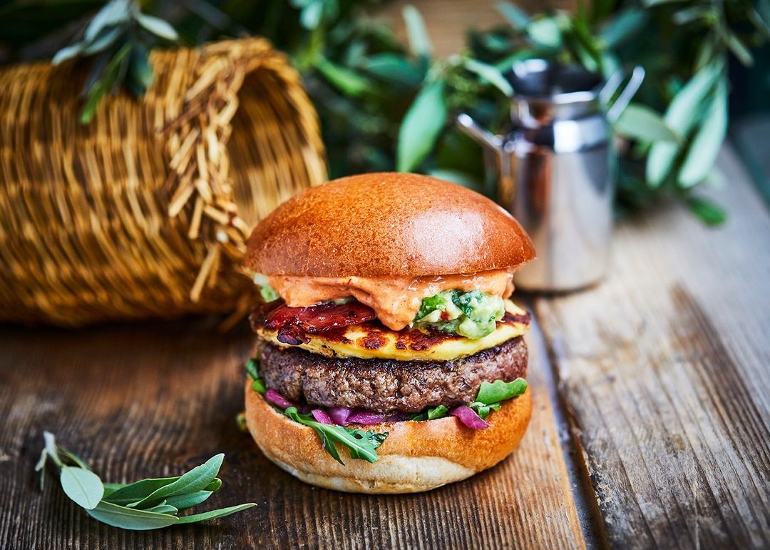 Overhead shot of a gourmet burger with toppings on a wooden surface, featuring fresh greens and a rustic presentation.