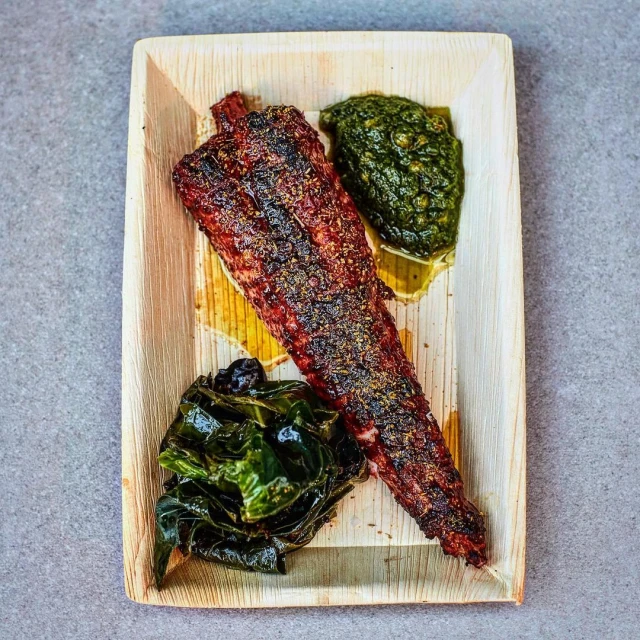 Grilled fish fillet served with green sauce and leafy greens on a palm leaf plate, presenting a visually appealing culinary dish.